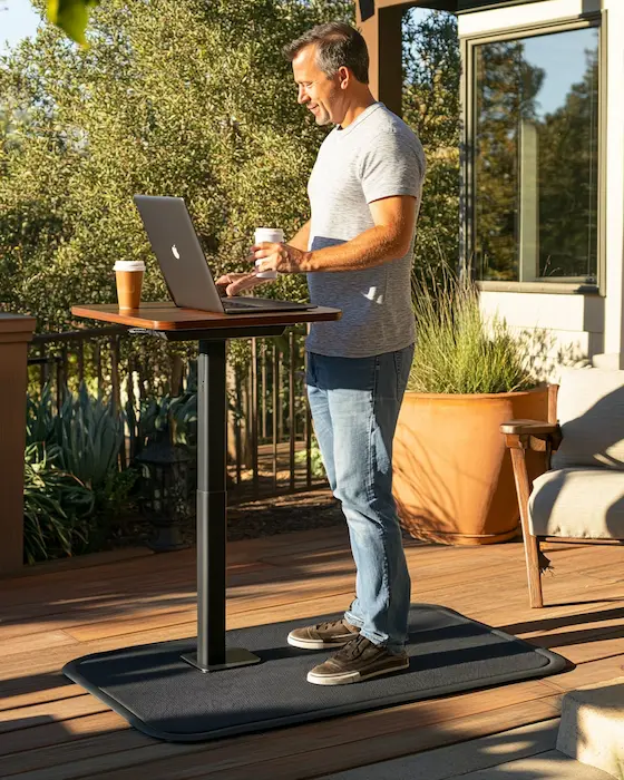 Man werkt staand op een terras met laptop en koffie op een verstelbaar bureau