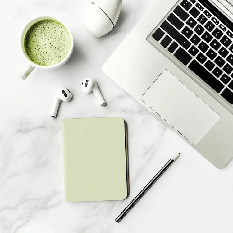 Wit bureau met laptop, matcha latte, oordopjes en notitieboekje voor een georganiseerde thuiswerkplek