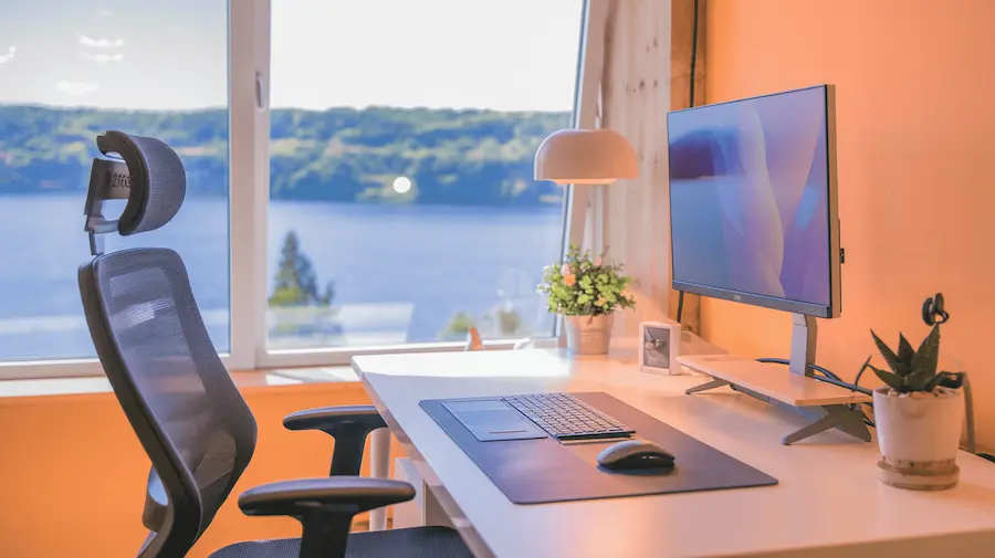 Ergonomisch thuiskantoor met comfortabele bureaustoel en monitor, uitzicht op water en daglicht.