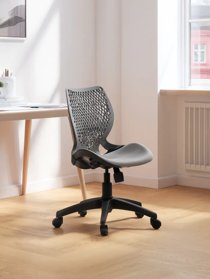 Een strakke zwarte ergonomische bureaustoel met geperforeerde rugleuning, geplaatst in een heldere, minimalistische kamer naast een houten bureau en witte muren.